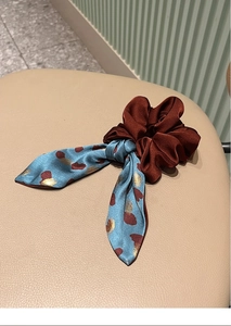 Close-up of burgundy satin scrunchie with light blue floral ribbon on leather surface