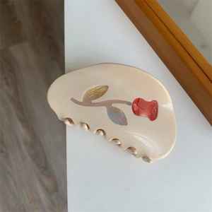 Detail of a beige acetate hair claw featuring a red rose pattern and pearlescent leaves