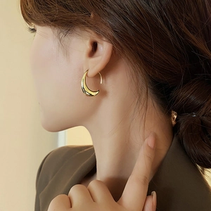 Close-up of a minimalist gold teardrop earring worn by a model in natural light