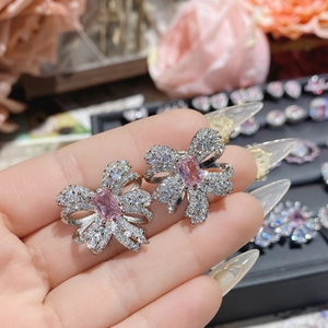 Macro shot of silver bow earrings featuring a pink gemstone and white zircon pavé setting