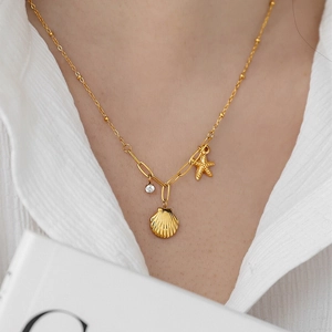 Gold necklace with shell and starfish charms worn by model over a white linen shirt