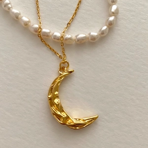 Close-up of golden crescent moon pendant with hammered texture and pearl strand necklace