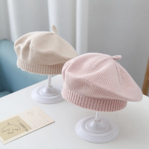 Beige and pink knitted baby beret hats for boys and girls shown on white stands