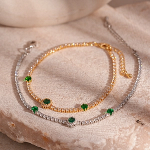 Vintage style gold and silver tennis bracelets with emerald green zircons on stone surface