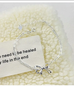 Detail of silver bow bracelet with rectangular links and heart charm on soft plush