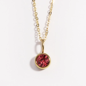 Close-up of a gold necklace with a round red birthstone pendant on a white background