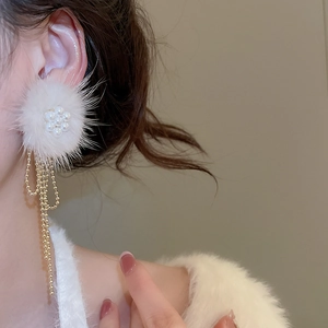 Detail of long plush pearl drop earrings with white pom-pom and gold tassels