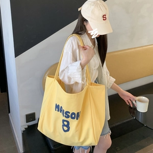 Detailed view of yellow canvas tote bag with MAISON 8 print worn by a fashion model