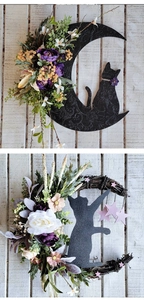 Close-up of crescent moon cat wreath with purple flowers on white wooden wall