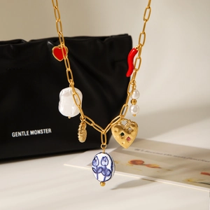 Gold chain necklace with red heart, baroque pearl, and ceramic charms on a black bag