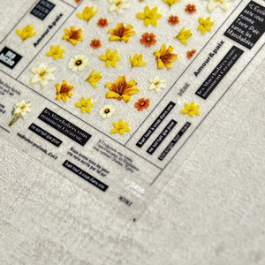 Artistic floral nail decals with yellow lilies and vintage text labels on linen