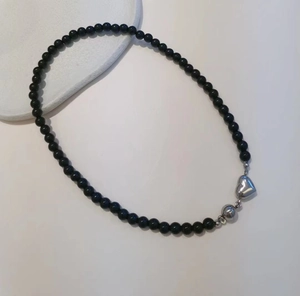 Detail shot of black beaded necklace with silver heart pendant on white background