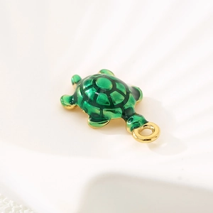 Close-up of golden turtle pendant with green enamel inlay on a white shell background