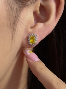 Macro shot of rectangular yellow gemstone stud earring with white diamond halo on ear