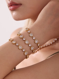 Detail of model wearing layered gold necklaces and halo-set cubic zirconia bracelets