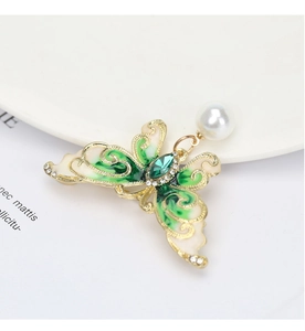 Detail of butterfly brooch with green enamel wings, crystal accents and a white pearl drop