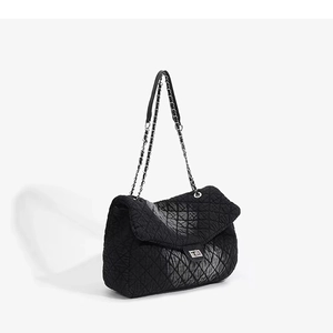 Close-up of black quilted shoulder bag with silver chain strap and square metal clasp