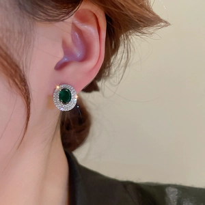 Close-up of emerald green oval stud earrings with pavé zircon details on a model's ear