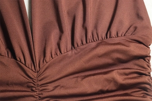 Macro detail of dark brown pleated knit fabric on a deep V-neck sleeveless dress