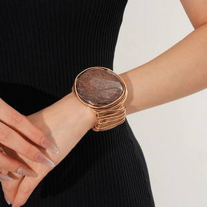 Detail of a large gold wire-wrapped bracelet featuring a brown resin stone on a model's arm