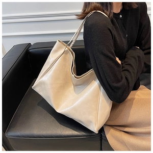 Detail view of a large beige soft leather tote bag held by a model on a black sofa
