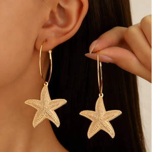 Boucles d'oreilles créoles étoile de mer dorées avec pendentifs marins portées par mannequin