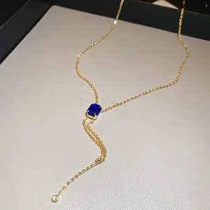 Macro detail of Y-shaped gold necklace with emerald-cut blue gemstone and drop chain