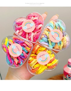 Macro shot of colorful elastic kids hair ties in heart-shaped clear storage gift boxes