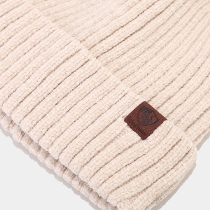 Détail d'un bonnet en tricot beige avec écusson en cuir marron et texture douce