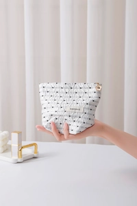 Dettaglio della borsa da trucco bianca a pois con texture a pieghe e zip a fiore