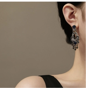 Detailed view of vintage silver earrings with dark blue gemstone and tassel on model