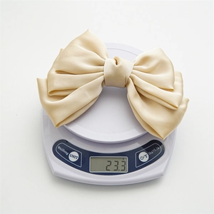 Close-up of a layered beige satin bow hair clip weighing 23.3g on a digital scale