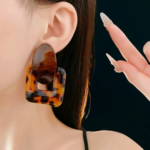 Detailed view of large square tortoise shell resin earrings on model with black background