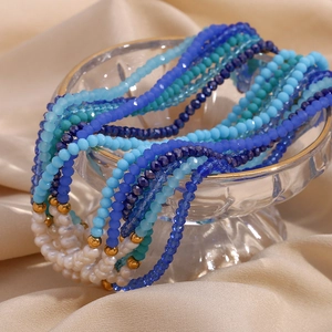 Close-up of blue faceted beads and freshwater pearls draped over a glass on silk fabric