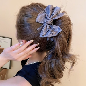 Close-up of a grey denim bow hair clip with black ribbon patterns on a brunette ponytail
