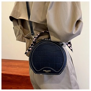 Detail of black round shoulder bag with crocodile texture and pink checkered scarf handle