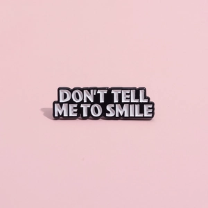 Funny black enamel pin badge with white text DON'T TELL ME TO SMILE on pink background