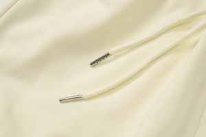 Détail macro du tissu en coton crème et des embouts de cordon argentés sur le pantalon