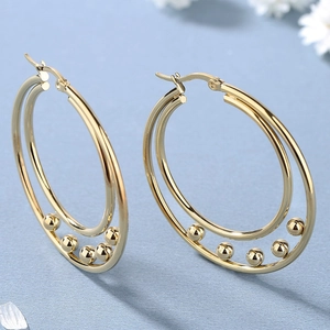 Fashionable gold double hoop earrings with metal beads on light blue textured background