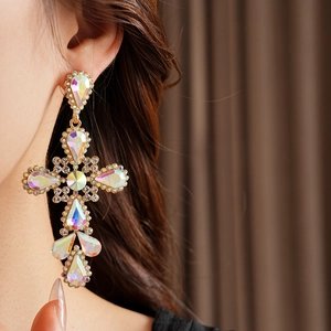Close-up of vintage gold cross earrings with iridescent rhinestones worn by a model