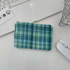 Petit porte-monnaie en tissu à carreaux bleu et vert sur un bureau blanc épuré