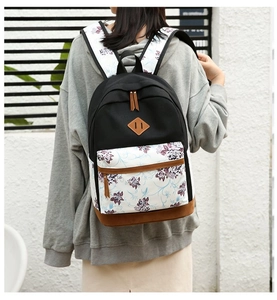 Floral backpack with purple prints and leather bottom worn by model against a white wall