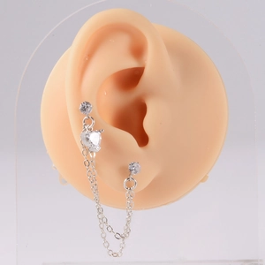 Detail of silver double-piercing chain earrings with heart-shaped zircon on a silicone ear