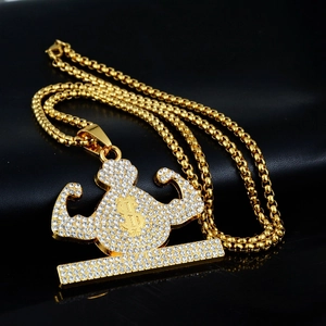 Detail of gold-plated hip hop pendant with rhinestones featuring dollar sign and muscle arm