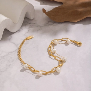Elegant gold stainless steel layered bracelet with fresh water pearls on marble background