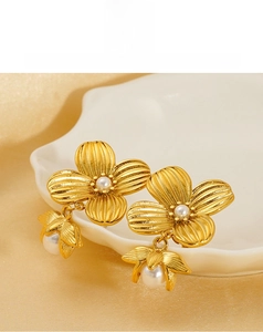 Detail of gold floral pearl earrings featuring layered petals on a white shell plate