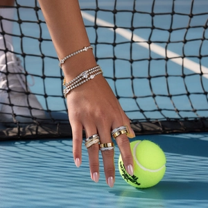 Close-up of stacked gold and silver rings with white zircon stones on a tennis court