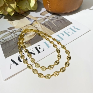 Detailed view of golden coffee bean link chain layered on a white surface and magazine