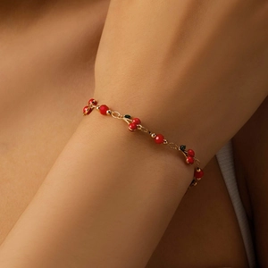 Golden chain bracelet featuring red beaded cherries and green leaves on a model wrist