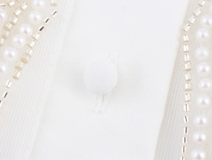 Detailed view of white fabric with fabric-covered button and delicate pearl bead embroidery